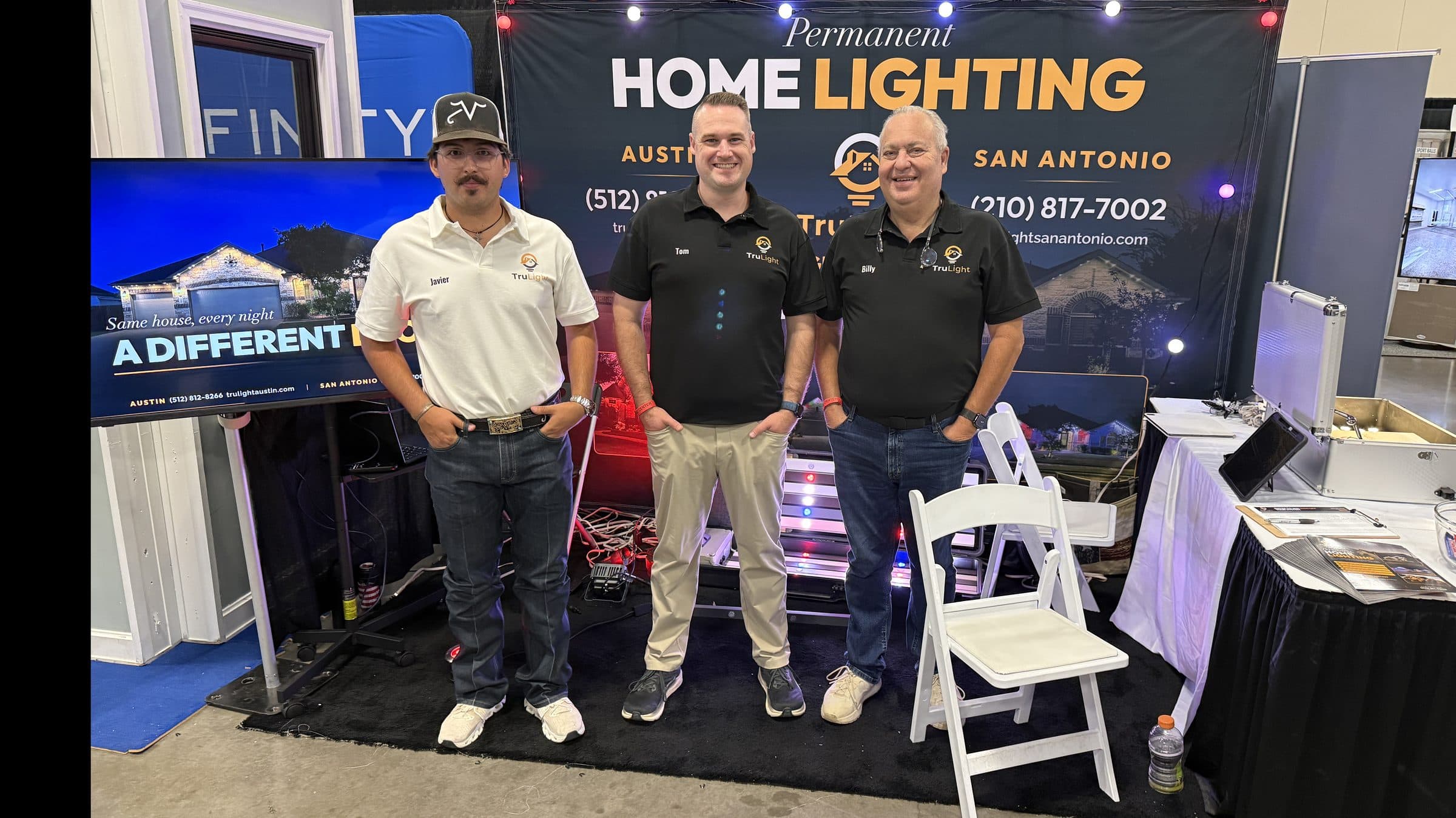 Javier Vargas, Tom Porter, and Billy Niels standing at the TruLight booth in front of the Austin and San Antonio backdrop