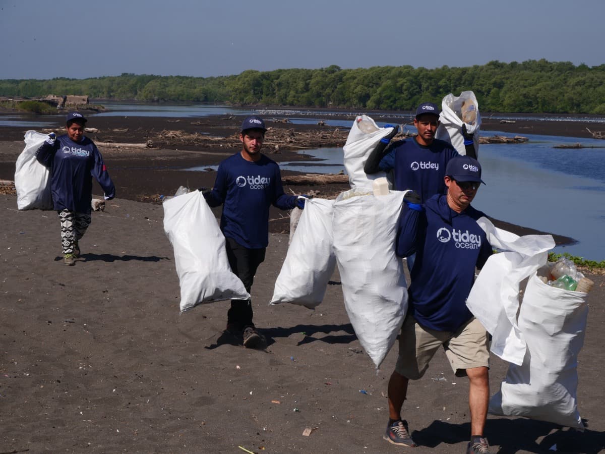 Tidey Ocean team carrying collected plastic on a beach cleanup