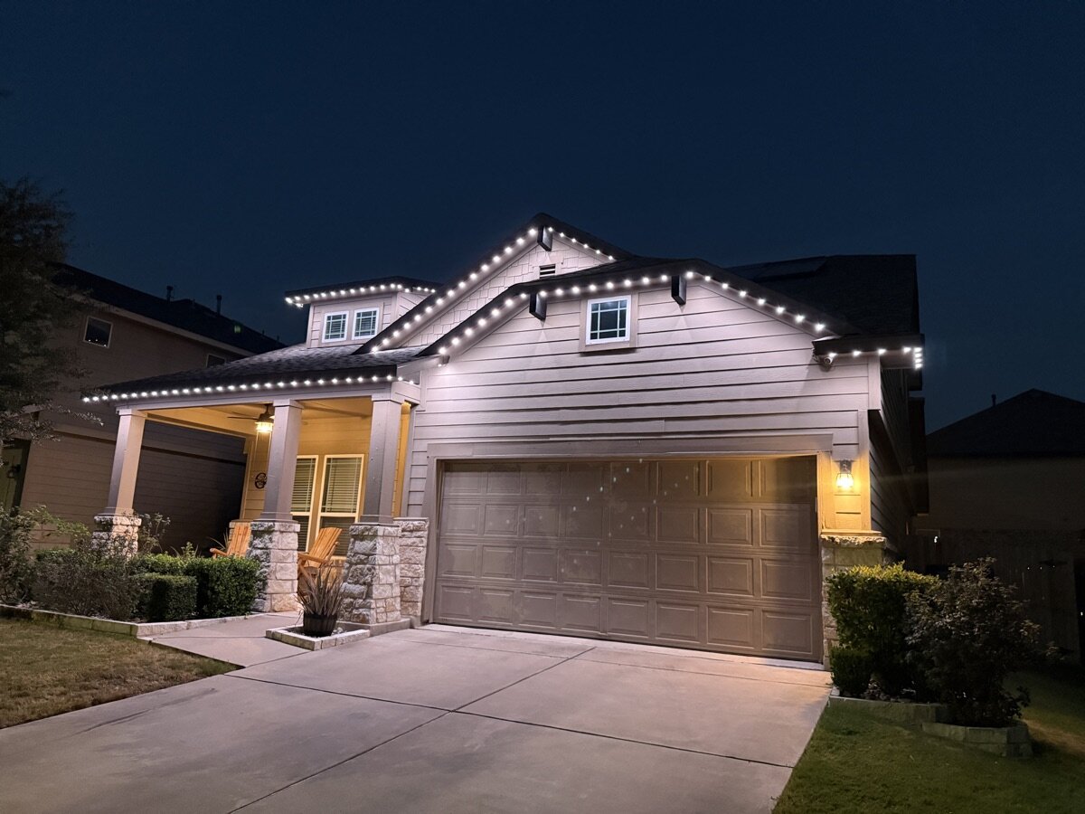 Pure white TruLight permanent lighting under the eaves of a two-story home with a stone porch (TruLight Austin install)